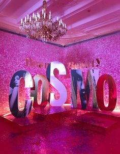 the word cosmo spelled out in front of a pink wall and chandelier