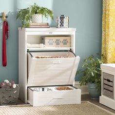 a white chest with two drawers and some plants in it next to a blue wall