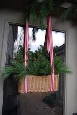 a basket filled with plants hanging from the side of a window next to a christmas tree