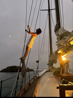 a man standing on the side of a sailboat at sunset with his arms outstretched