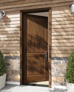 a wooden door is open in front of a brick building with potted plants on the sidewalk