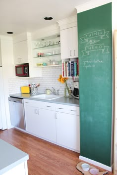 a kitchen with white cabinets and green chalkboard on the wall