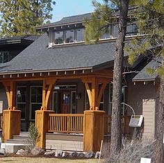 a house with wooden porchs and pillars in front of the building, surrounded by pine trees