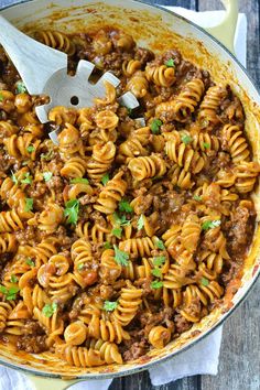 a skillet filled with pasta, meat and sauce on top of a wooden table