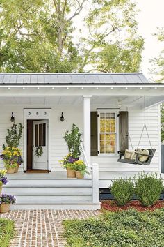 a small white house with potted plants on the front porch and steps leading up to it