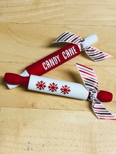 two candy canes with red and white ribbons on top of a wooden table next to each other