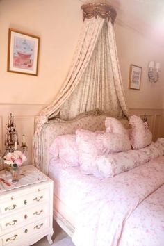 a bed with pink sheets and pillows on top of it next to a white dresser