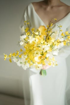 a woman in a white dress holding a bouquet of yellow and white flowers on her wedding day