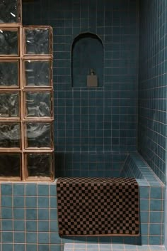 a bathroom with blue tiled walls and flooring, including a window in the shower