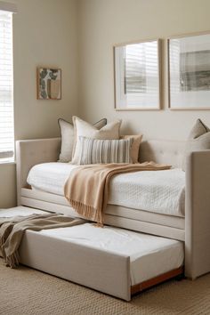 a white day bed sitting in a bedroom next to two framed pictures on the wall