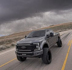 a silver truck driving down the road under a dark sky with clouds in the background