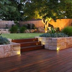 a wooden deck surrounded by plants and rocks with lights on the steps leading up to it