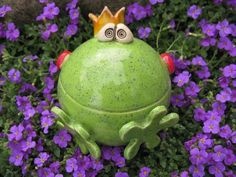 a frog statue with two eyes and a crown on its head sitting in purple flowers