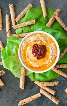 a white bowl filled with dip surrounded by crackers on top of a green leaf