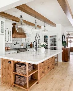 a large kitchen with white cabinets and wooden beams on the ceiling is decorated with baskets