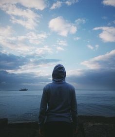 a person standing in the water looking out to sea with a boat in the distance