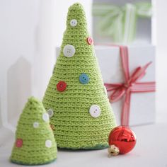 two crocheted christmas trees sitting next to each other with presents in the background