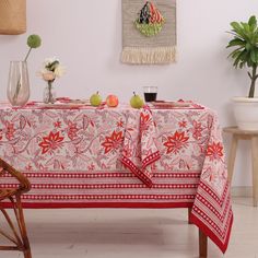 a red table cloth with flowers and fruit on it in front of a white wall