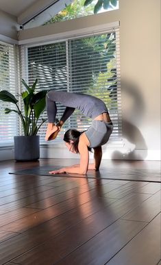 a woman is doing yoga on the floor in front of a potted plant and window