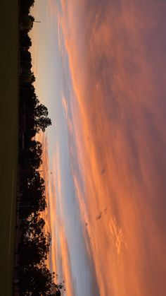 the sky is pink and orange as the sun sets in the distance behind some trees