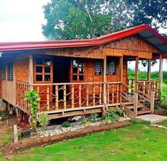 a small wooden house with red roof and balcony in the middle of a green field