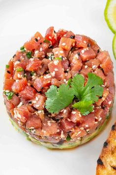 a white plate topped with a sandwich covered in meat and garnish next to slices of lime