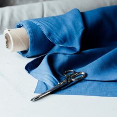 a pair of scissors on top of a blue cloth next to a roll of thread