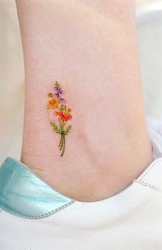 a small flower tattoo on the ankle that is being worn by a woman's foot