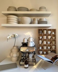 a coffee maker sitting on top of a white counter next to plates and mugs