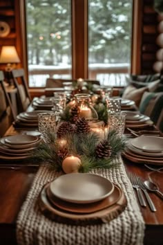 a dining room table set for christmas with candles and pine cones on the centerpiece