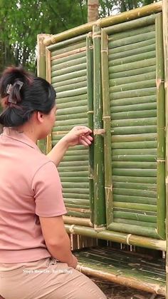 a woman sitting on the ground next to a green bamboo structure with closed shutters