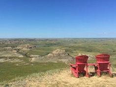 two red chairs sitting on top of a grass covered hill next to a valley filled with green hills