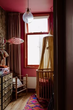 a baby crib next to a window in a room with pink walls and curtains