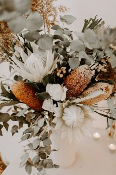 a vase filled with flowers and greenery on top of a white table cloth covered table