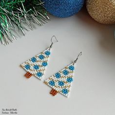 a pair of beaded christmas tree earrings sitting on top of a table next to ornaments