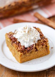 a white plate topped with a piece of cake covered in whipped cream and pecans