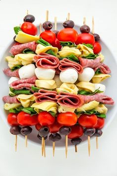 an appetizer platter with meats, olives and tomatoes on skewers