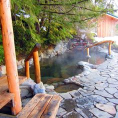 a wooden bench sitting on top of a stone walkway next to a small pond in the woods