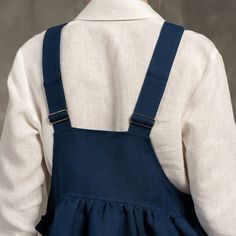 the back of a woman's dress with blue suspenders and white shirt on