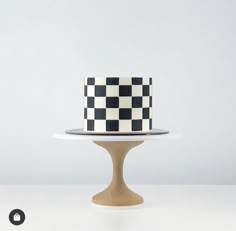 a black and white checkered cake sitting on top of a wooden stand next to a wall