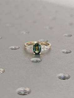 a green and white diamond ring sitting on top of a silver surface with lots of dots