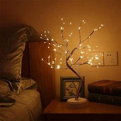 a small tree with white lights on it in a bedroom next to a night stand