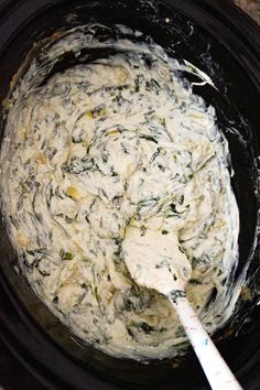 a black crock pot filled with cream cheese and spinach leaves, next to a spoon