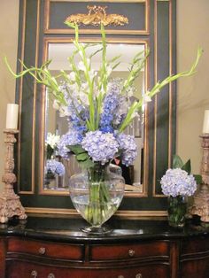 a vase filled with blue and white flowers on top of a wooden dresser next to a mirror