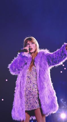 a woman in a purple fur coat on stage with her hands out to the side