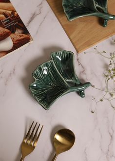 two forks, spoons and a book on a marble counter top next to flowers