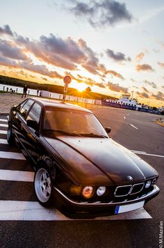 a black car parked in the middle of an empty parking lot at sunset or dawn