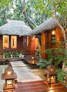 a small wooden house surrounded by greenery and lit up lanterns in the front yard