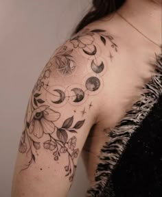 a woman's shoulder with flowers and moon tattoos on her left arm, which is covered in black ink