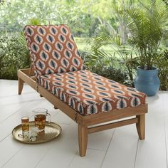 a chaise lounge chair with an orange and blue patterned cover on it, next to a potted plant